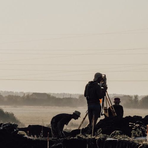 Group of surveyors using a theodolite at a construction site during a foggy morning with silhouettes visible.